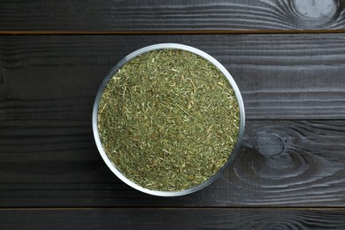Photo of Bowl with dried dill on black wooden table, top view