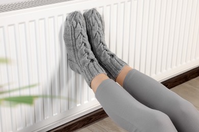 Photo of Woman warming feet near heating radiator indoors, closeup