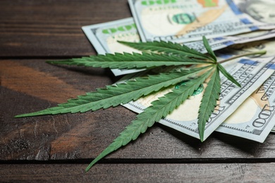 Photo of Hemp leaf and dollars on wooden background, closeup