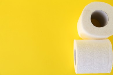 Photo of Soft toilet paper rolls on yellow background, top view. Space for text