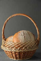 Photo of Wicker basket with fresh bread on grey wooden table