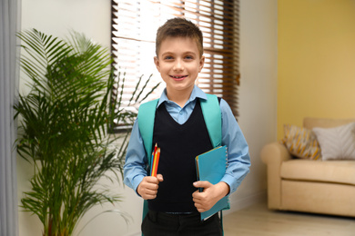 Photo of Little boy in uniform with school stationery at home