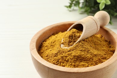 Photo of Dry curry powder in bowl and scoop on light wooden table, closeup. Space for text