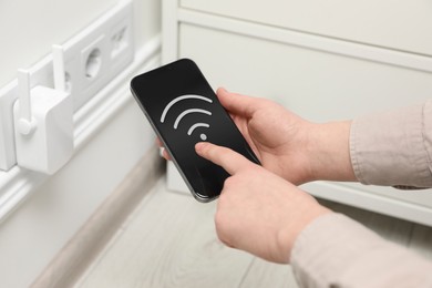 Image of Woman with smartphone connecting to internet via wireless repeater indoors, closeup. Wi-Fi symbol on device screen