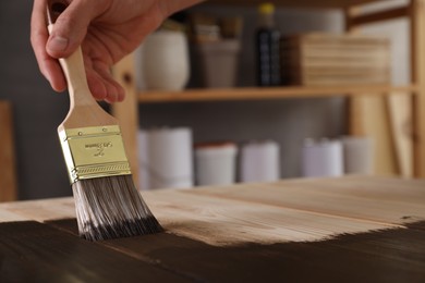 Photo of Man with brush applying wood stain onto wooden surface indoors, closeup. Space for text