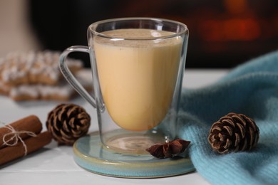 Photo of Tasty eggnog, anise star and cones on white wooden table, closeup