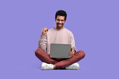 Photo of Happy man with laptop sitting on purple background