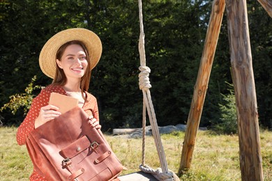 Photo of Beautiful young woman taking book from bag outdoors on sunny day. Space for text
