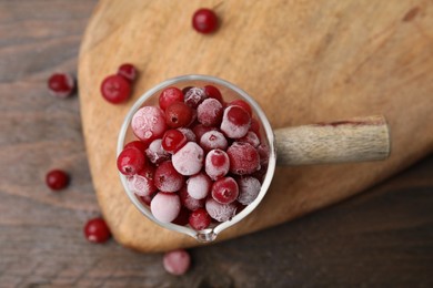 Photo of Frozen red cranberries in glass pot on wooden table, top view