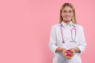 Photo of Doctor with stethoscope holding pink ribbon on color background, space for text. Breast cancer awareness