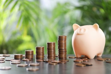 Photo of Stacked coins and piggy bank on grey table against blurred green background. Space for text