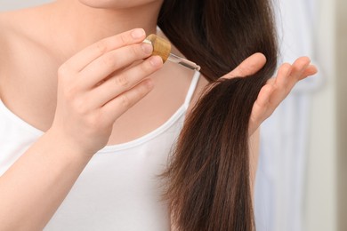 Photo of Woman applying essential oil onto hair on blurred background, closeup