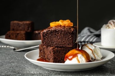 Photo of Pouring sauce onto ice-cream with fresh brownies on plate. Delicious chocolate pie