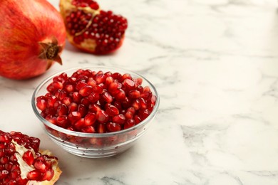 Photo of Ripe juicy pomegranate grains in bowl on white marble table, space for text