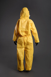 Photo of Woman wearing chemical protective suit on grey background, back view. Virus research