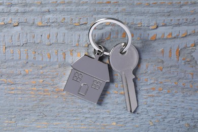 Photo of Key with keychain in shape of house on grey wooden table, top view