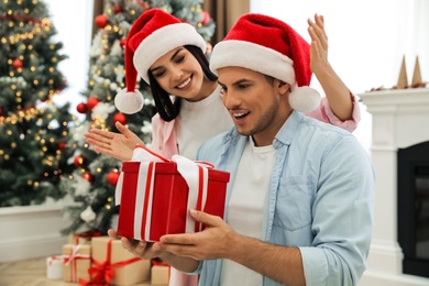 Photo of Happy couple in Santa hats with Christmas gift at home