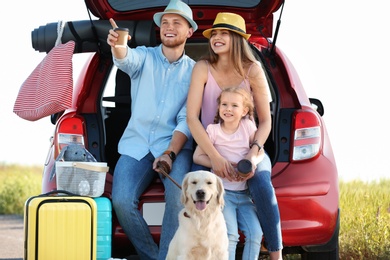 Photo of Young family with luggage and dog near car trunk outdoors