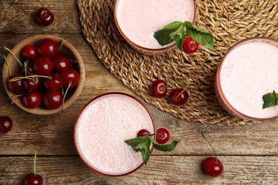 Photo of Tasty fresh milk shakes with cherries on wooden table, flat lay