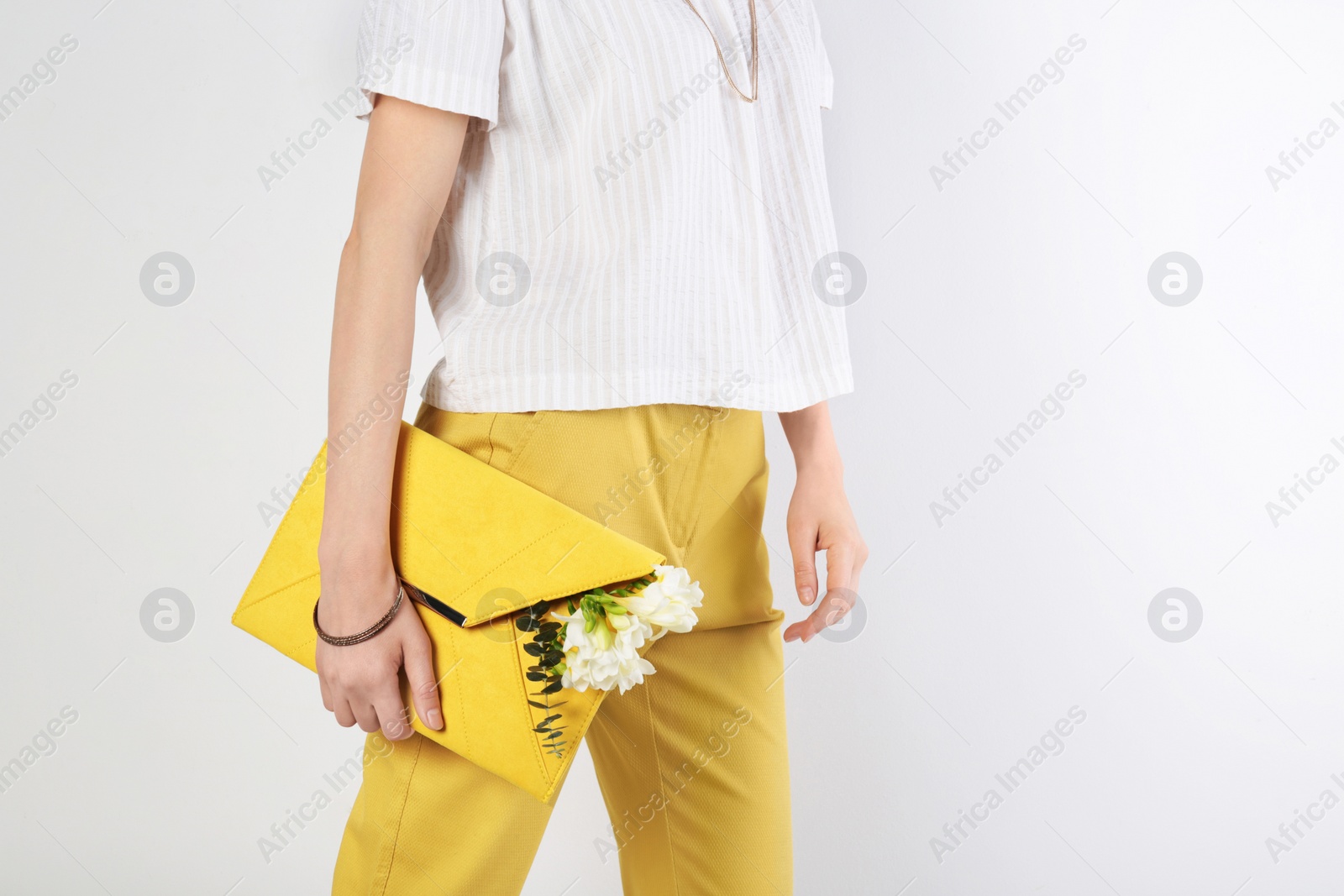 Photo of Stylish woman with clutch and spring flowers against light background, closeup