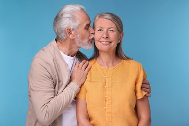 Photo of Senior man kissing his beloved woman on light blue background