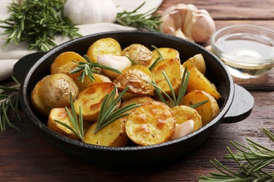 Photo of Delicious baked potatoes with rosemary in frying pan on wooden table, closeup