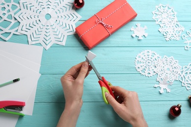 Photo of Woman making paper snowflake at turquoise wooden table, top view