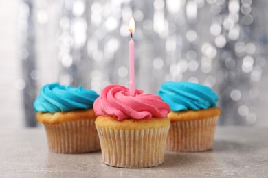 Photo of Delicious cupcakes with bright cream and burning candle on grey table, closeup