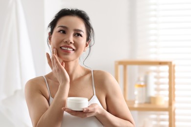 Photo of Happy woman applying face cream at home