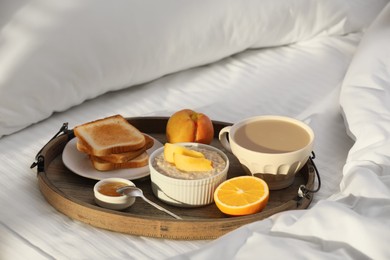 Photo of Wooden tray with delicious breakfast on bed in morning