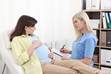 Photo of Doctor with clipboard consulting pregnant patient in clinic