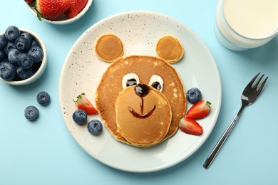 Photo of Creative serving for kids. Plate with cute bear made of pancakes and berries on light blue table, flat lay