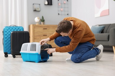 Photo of Travel with pet. Man closing carrier with cat at home