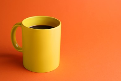 Photo of Yellow mug of freshly brewed hot coffee on orange background, space for text