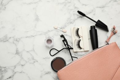 Photo of Cosmetic bag with eyelash curler and makeup products on white marble table, flat lay. Space for text