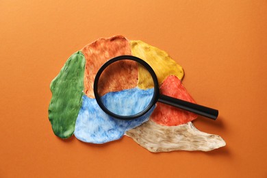 Photo of Amnesia problem. Magnifying glass and brain with sections on orange background, top view