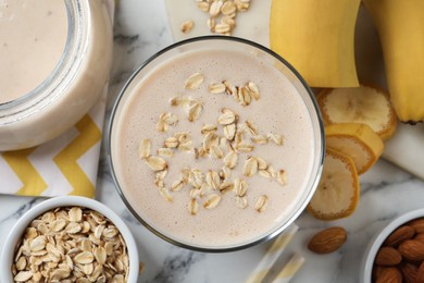 Photo of Glass of tasty banana smoothie with oatmeal on white marble table, flat lay