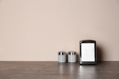 Photo of Napkin holder with salt and pepper shakers on table against color background. Space for text