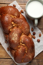 Photo of Delicious yeast dough cake, nuts and cup of milk on wooden table, flat lay