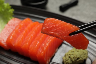 Photo of Taking tasty salmon slice with chopsticks from plate, closeup. Delicious sashimi dish