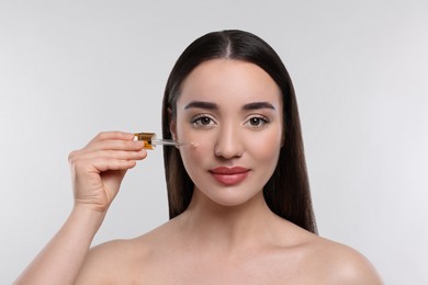 Photo of Young woman applying essential oil onto face on light grey background