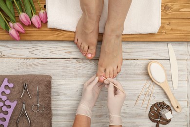 Photo of Professional pedicurist working with client`s toenails in beauty salon, top view