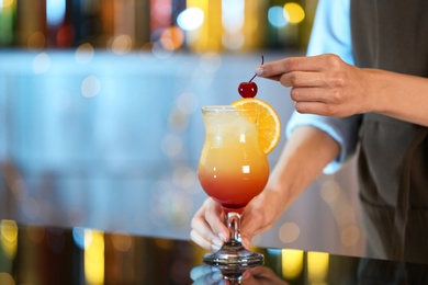 Bartender decorating glass of fresh alcoholic cocktail at bar counter