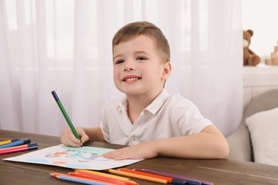 Photo of Cute little boy drawing with pencil at wooden table in room. Child`s art