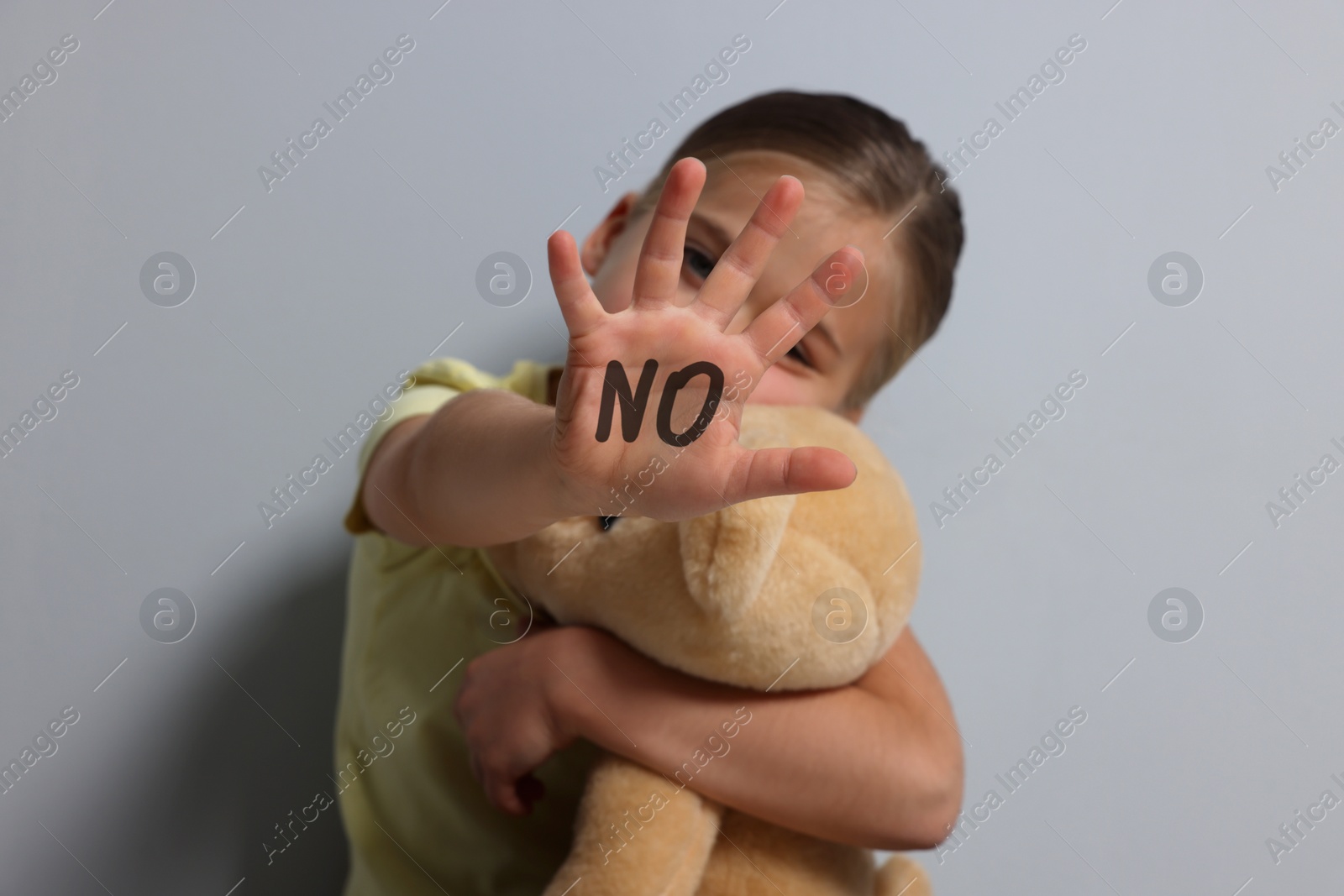 Image of Child abuse. Girl with toy making stop gesture near grey wall, selective focus. No written on her hand
