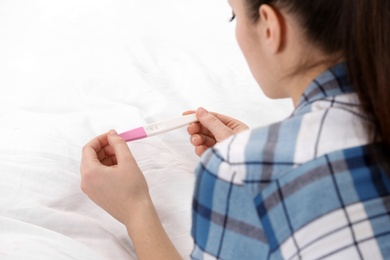 Photo of Young woman with pregnancy test on bed, closeup. Gynecology and childbirth