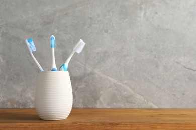Photo of Plastic toothbrushes in holder on wooden table, space for text