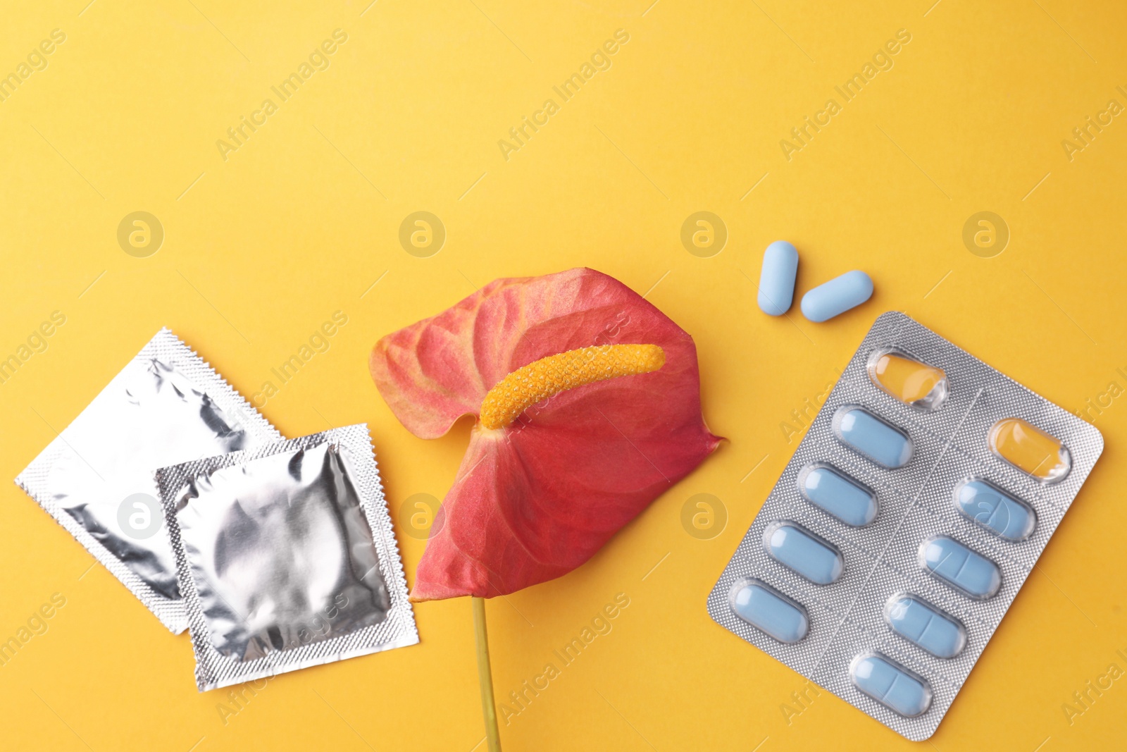 Photo of Anthurium flower symbolizing male sexual organ, pills and condoms on orange background, flat lay. Potency problem