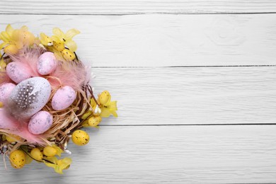 Photo of Festively decorated Easter eggs on white wooden table, top view. Space for text