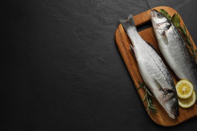 Photo of Tasty sea bass fish on black textured table, top view. Space for text